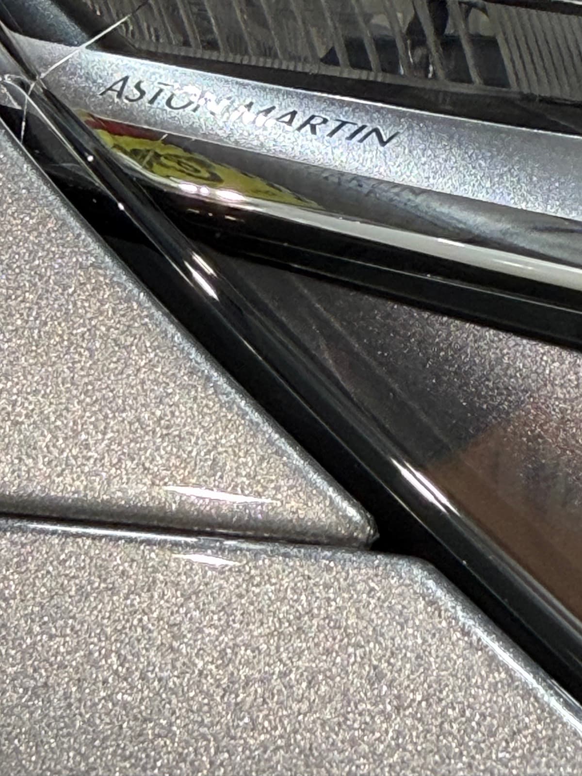 Aston Martin rear badge macro on silver metallic paint with the Ferrari flag reflected in the gloss through clear STEK PPF