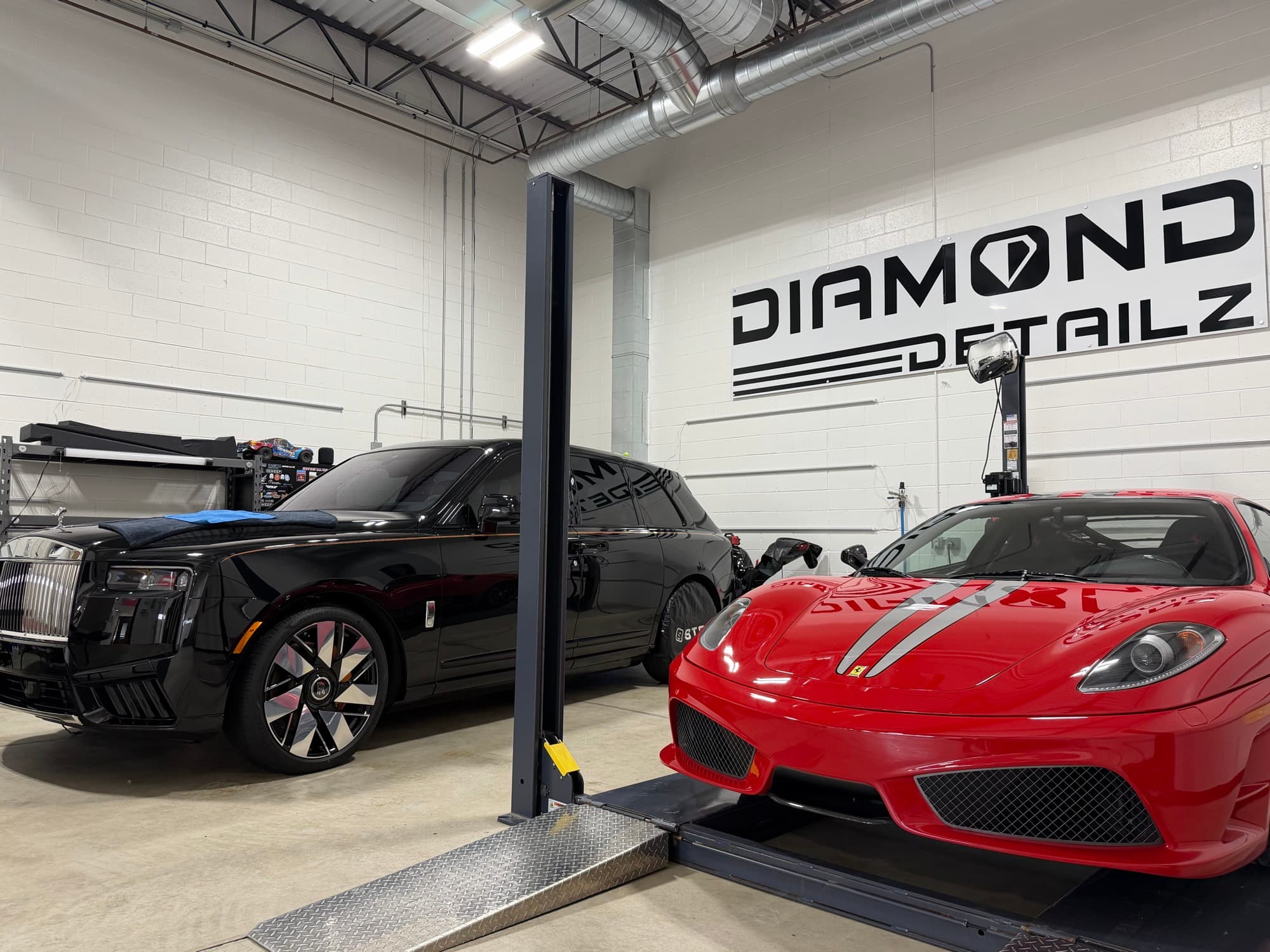 Rolls Royce Cullinan and Ferrari F430 Scuderia side by side in the Diamond Detailz install bay with the Diamond Detailz logo on the back wall